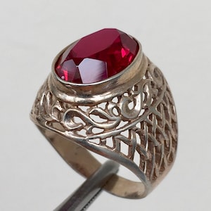 Puede incluir: Un anillo de plata con una piedra preciosa roja engastada en un diseño de filigrana.