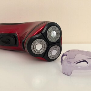 May include: A red electric razor with a three-blade head and a clear plastic cover.
