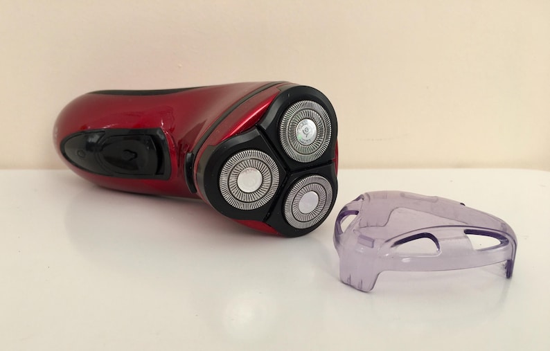May include: A red electric razor with a three-blade head and a clear plastic cover.