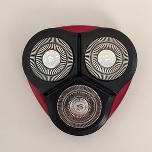 May include: Close-up of a black electric razor head with three silver blades. The blades have the text "shaver.com.ua" printed on them.