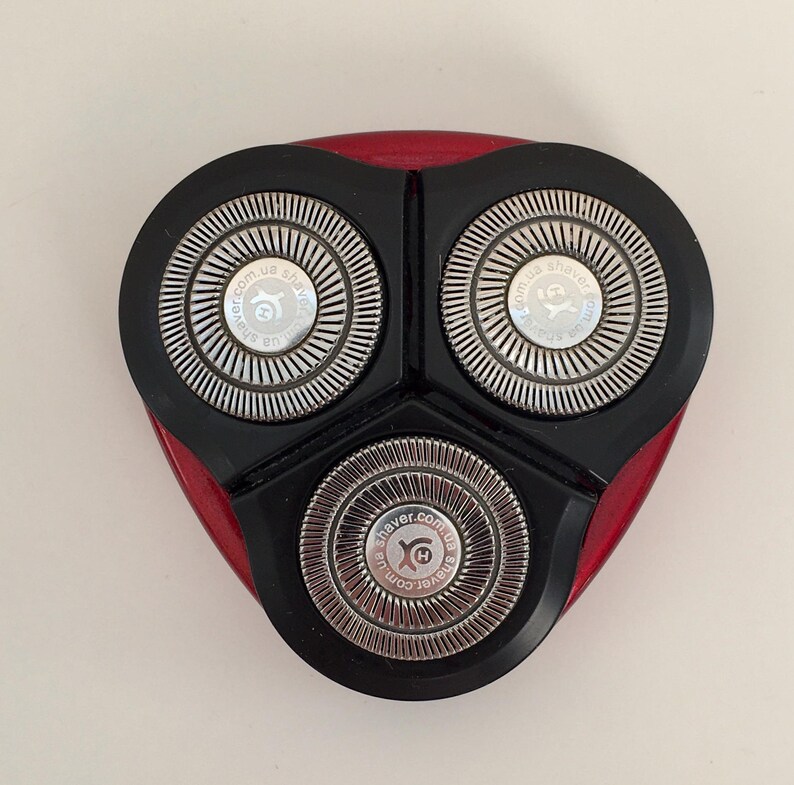 May include: Close-up of a black electric razor head with three silver blades. The blades have the text "shaver.com.ua" printed on them.