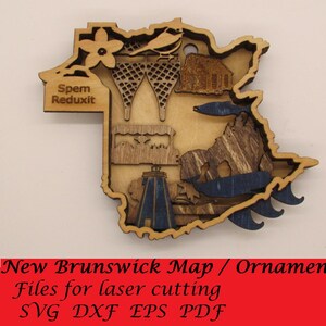 May include: A wooden ornament in the shape of New Brunswick, Canada, with laser-cut details. The ornament features a lighthouse, snowshoes, and other regional symbols. The text "Spem Reduxit" is visible. The bottom of the image has the text "New Brunswick Map / Ornament".