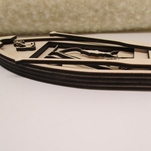 May include: A wooden cutout of a boat with oars, featuring an anchor design. The boat is layered and has a brown stain.