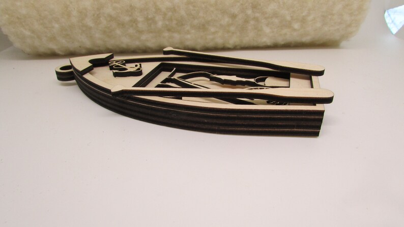 May include: A wooden cutout of a boat with oars, featuring an anchor design. The boat is layered and has a brown stain.