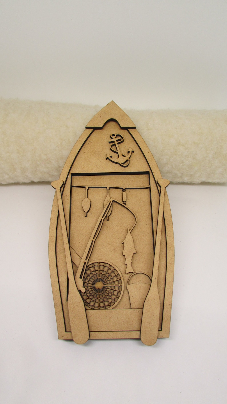May include: Wooden cutout of a boat with fishing gear, including a fishing rod, net, bucket, and fish. The boat has an anchor at the top and two oars on the sides.