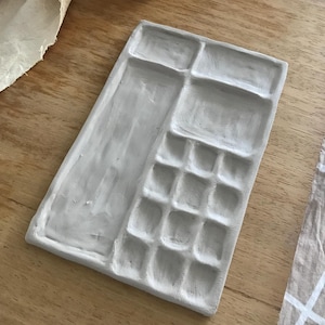 May include: A gray ceramic palette with 16 individual wells for mixing paint. The palette is rectangular and has a textured surface.