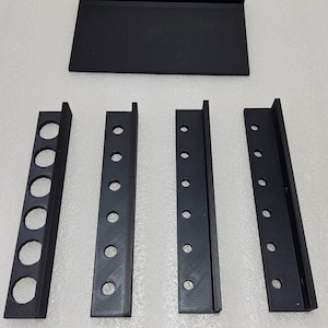 May include: A set of four black plastic wall-mounted organizers with multiple round holes. The organizers are designed to hold tools or other small items.