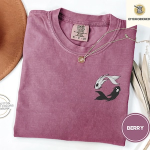 May include: A maroon t-shirt with a black and white fish design. The shirt is made of 100% cotton and is pre-shrunk. The text "COMFORT COLORS" is printed on the tag.