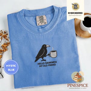 May include: Mystic blue t-shirt featuring a black crow with a coffee cup and the text "Hello Darkness My Old Friend". The shirt has a Comfort Colors tag.