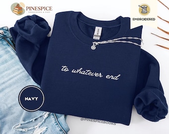 May include: Navy blue sweatshirt with the embroidered phrase "to whatever end." A silver necklace with a circular pendant rests on the sweatshirt. The word "NAVY" is in a navy circle. The sweatshirt is folded over a pair of blue jeans.