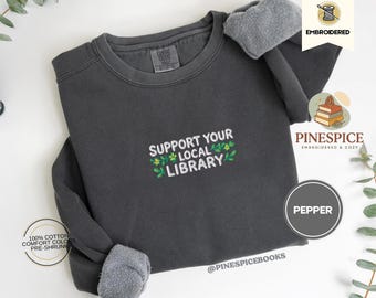 Peut inclure: Un sweat-shirt gris foncé avec le texte brodé "SUPPORT YOUR LOCAL LIBRARY" en blanc, vert et jaune. Le sweat-shirt est en 100% coton et est pré-rétréci. La couleur est "Pepper".