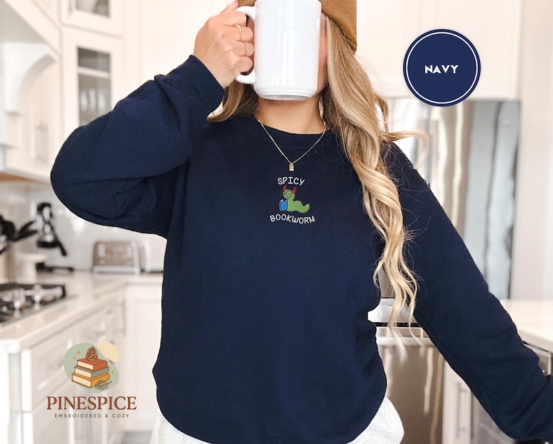Puede incluir: Sudadera azul marino con dise&ntilde;o bordado "Spicy Bookworm". El dise&ntilde;o presenta un gusano verde con un chile rojo. La sudadera es de manga larga y cuello redondo.