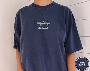 May include: A navy blue t-shirt with a green vine and sword graphic and the text "You do not yield".