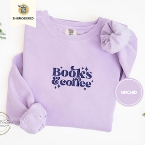Op de afbeelding: Een lavendelkleurig sweatshirt met de tekst "Books & Coffee" in donkerblauwe letters. Het sweatshirt is geborduurd en heeft een ontspannen pasvorm.