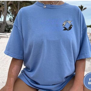May include: A light blue t-shirt with a graphic of two fish swimming in a circle. The fish are black and white. The shirt is made of a soft, comfortable material.