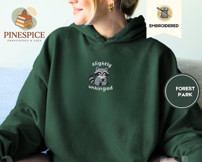Pu&ograve; includere: Felpa con cappuccio verde scuro con un design ricamato di procione. Il procione &egrave; grigio e nero, con le parole "slightly unhinged" sopra e sotto. La felpa ha un cappuccio con coulisse e una tasca a marsupio.