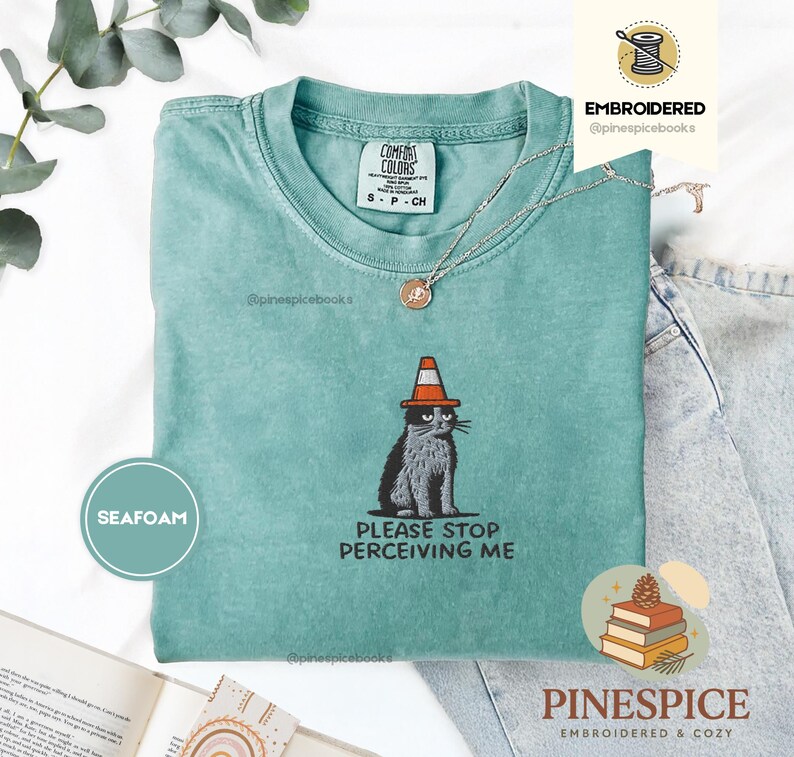 May include: Seafoam green t-shirt with a graphic of a cat wearing a traffic cone hat. The cat is black and gray, with the text "PLEASE STOP PERCEIVING ME" below. The shirt is from Comfort Colors and is size small.