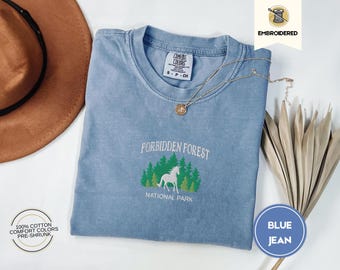 Puede incluir: Una camiseta de mezclilla azul con un diseño bordado de un caballo blanco en un bosque con el texto "Forbidden Forest National Park".