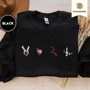 May include: Black sweatshirt with embroidered symbols, including a hand holding an apple, a leaf, a snake, a chess piece, and a chessboard. The text "EMBROIDERED" is visible in the top right corner.