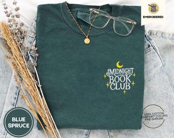 Peut inclure: Un t-shirt vert foncé avec le texte "Midnight Book Club" brodé en jaune sur le devant. Le texte est entouré de petites étoiles jaunes.