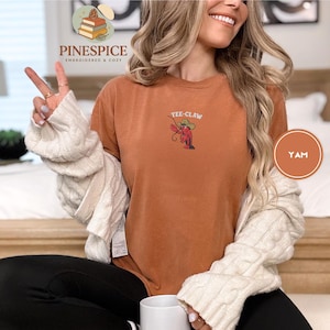 May include: A burnt orange t-shirt with the embroidered text "Yee-Claw" above a cartoon lobster wearing a cowboy hat. The shirt is part of the Pinespice collection, embroidered and cozy.