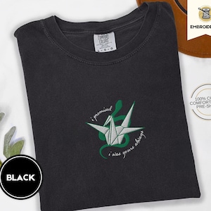 Op de afbeelding: Zwart T-shirt met een groene geborduurde origami-kraanvogel en de tekst "I promised I was yours always".