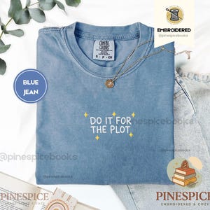 May include: A blue jean colored crew neck t-shirt with white embroidered text that reads DO IT FOR THE PLOT, accented by small yellow embroidered stars. The shirt features a Comfort Colors brand label at the inner neckline and short sleeves.
