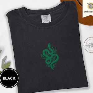 May include: Black t-shirt with an embroidered green snake design. The snake is surrounded by leaves and flowers. The shirt is made of 100% cotton and is pre-shrunk.