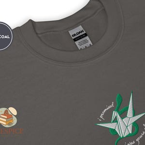 K&ouml;nnte beinhalten: Anthrazitfarbenes Sweatshirt mit Rundhalsausschnitt. Es hat ein gesticktes Origami-Kranich-Design in Wei&szlig; und Gr&uuml;n mit dem Text "i promised i was yours always". Das Markenlogo "Pinespice" ist ebenfalls sichtbar.
