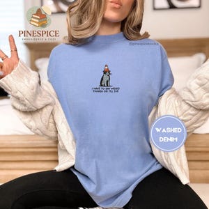 May include: A light blue washed denim sweatshirt with the text "I HAVE TO SAY WEIRD THINGS OR I'LL DIE". The sweatshirt features a graphic of a cat wearing a traffic cone hat. The brand name "PINESPICE" is at the top.