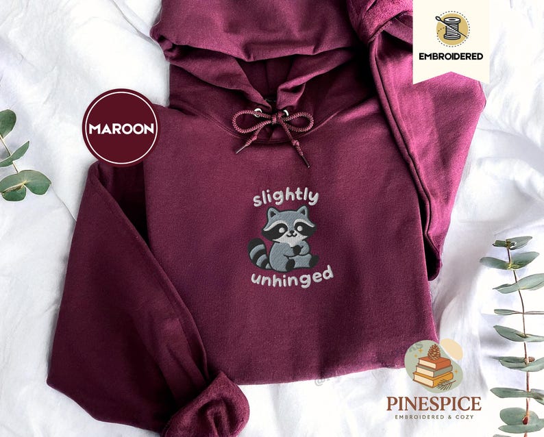 Pu&ograve; includere: Felpa con cappuccio bordeaux con cappuccio con coulisse e tasca a marsupio. La parte anteriore presenta una grafica ricamata di procione con le parole "slightly unhinged". La felpa con cappuccio &egrave; di Pinespice, ricamata e accogliente.