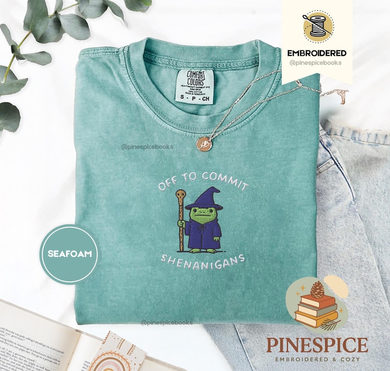 May include: Seafoam green t-shirt with the text "OFF TO COMMIT SHENANIGANS" and an embroidered frog wearing a wizard hat and robe. The shirt is a Comfort Colors brand, size S-CH.