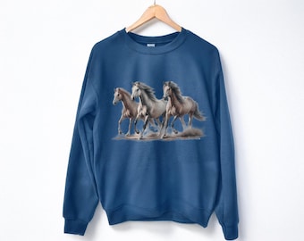 May include: A dark blue crewneck sweatshirt featuring a graphic print of three white horses galloping across a dusty ground. The horses are depicted in motion with flowing manes and tails, centered on the front of the long-sleeved pullover garment.