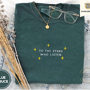 May include: A dark green t-shirt with the text "To the stars who listen" embroidered in white with yellow stars. The shirt is made of 100% cotton and is pre-shrunk.
