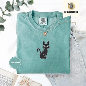 Camiseta Jiji Black Cat Bordada Comfort Colors®: Camisa caprichosa de gato brujo: un ambiente acogedor y familiar para amantes de la lectura y sus compañeros felinos
