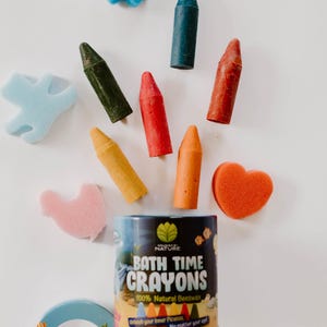 May include: A selection of bath time crayons and sponges in different colours and shapes. The crayons are in red, orange, yellow, green, and blue. The product is labelled "BATH TIME CRAYONS 100% Natural Beeswax".