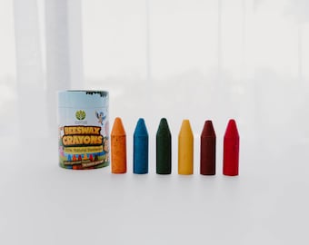 May include: A set of six colorful beeswax crayons in orange, blue, green, yellow, brown, and red, next to a cylindrical container. The container is light blue with the words "Beeswax Crayons" and "100% Natural Beeswax" printed on it.