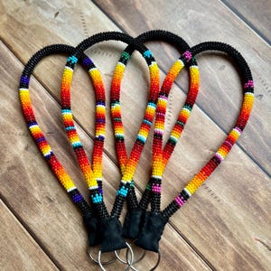 May include: Four beaded lanyards with a black cord and a colorful pattern of red, orange, yellow, and blue beads. Each lanyard has a black suede-like material at the bottom with a silver key ring attached.