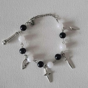 May include: A beaded bracelet featuring black and white beads, with silver-tone charms including a microphone, lightning bolt, sword, cross, and angel wing. The bracelet is on a light gray surface.