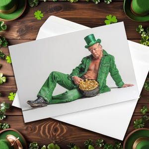 May include: A greeting card featuring a person in a green outfit, a leprechaun hat, and a pot of gold. The person is seated on a white surface. The card is inside a white envelope, with shamrocks and green hats in the background.