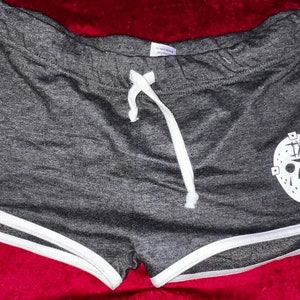 Puede incluir: Shorts deportivos grises con ribete blanco y un gráfico blanco de una máscara de hockey con el número "IX" en él.