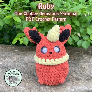 Op de afbeelding: Een gehaakte Ruby, een rood en zwart Pokémon-personage met een gele hoorn, zittend op een rots. Het yarnimal is een haakpatroon dat te koop is.
