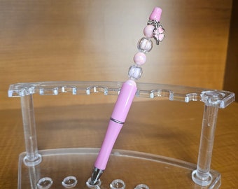 Bolígrafo rosa con dije de flor.