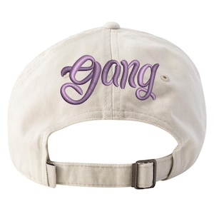 May include: A beige baseball cap with an embroidered purple "Gang" logo on the back.