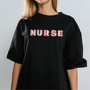 May include: Black t-shirt with the word "NURSE" printed in pink, blue and yellow letters.