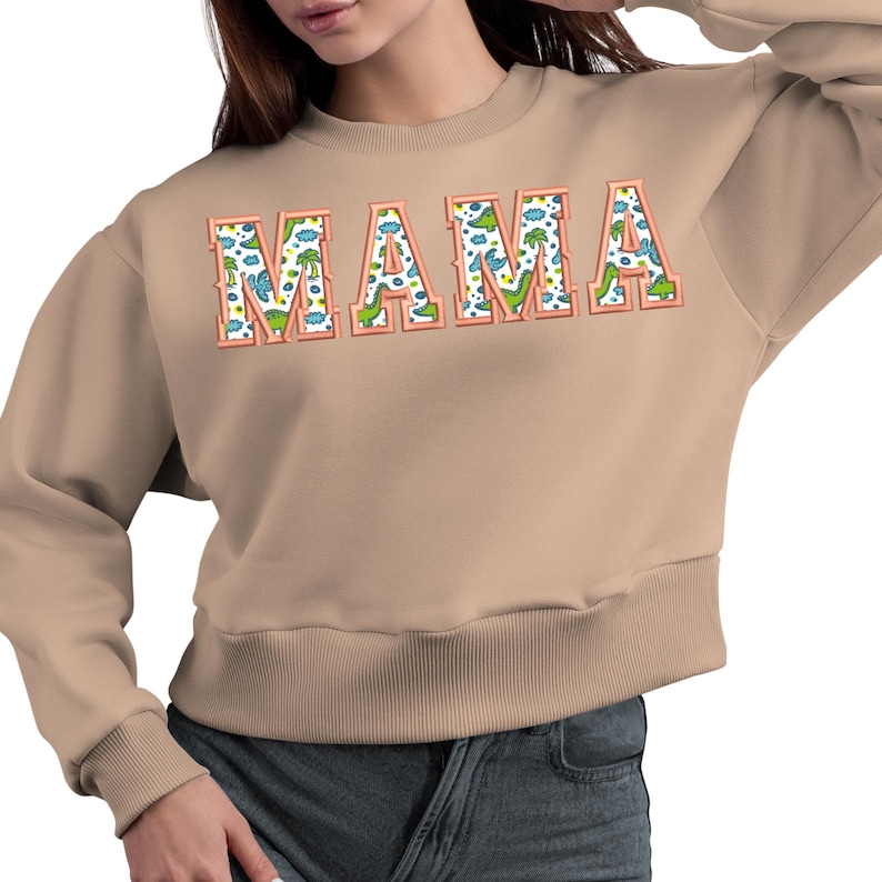 May include: A tan sweatshirt with a large graphic print of the word "MAMA" in a colourful dinosaur pattern.