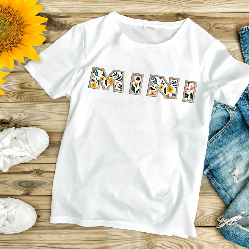 May include: White t-shirt with the word "MINI" spelled out in floral letters. The letters are outlined in brown and filled with a colourful floral pattern.