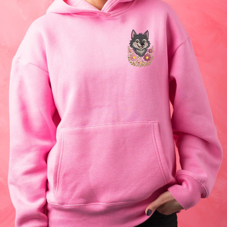 Puede incluir: Sudadera con capucha rosa con bolsillo delantero y capucha. La sudadera presenta un dise&ntilde;o bordado de la cabeza de un lobo rodeada de flores. El lobo es gris y negro, y las flores son rosas y amarillas.
