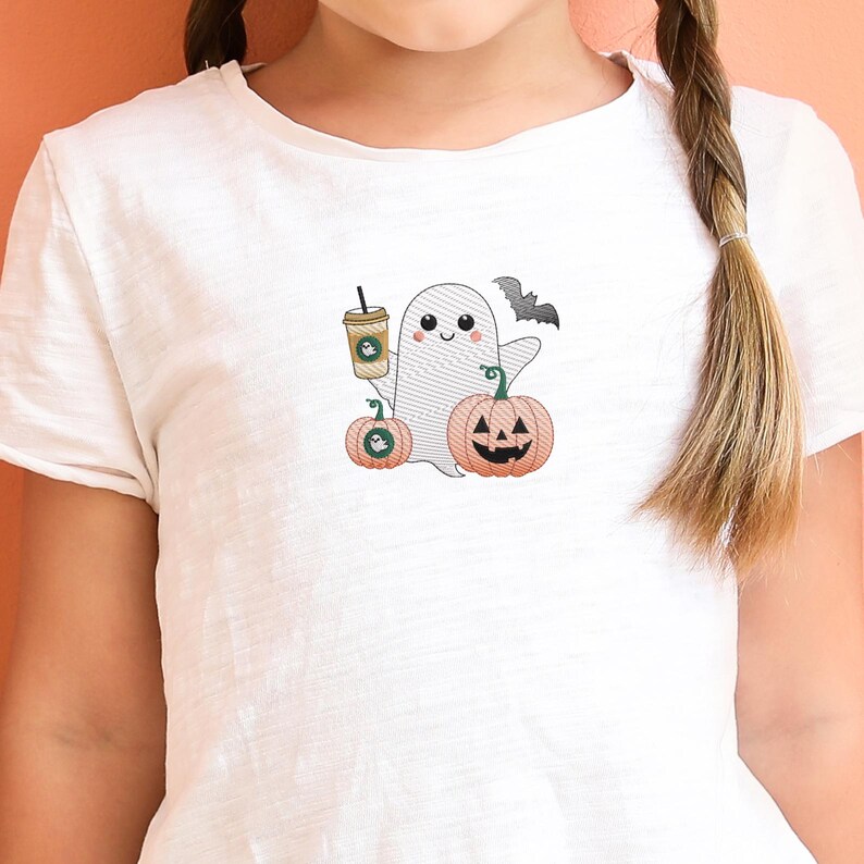 May include: White t-shirt with a cute ghost holding a pumpkin and a coffee cup. The ghost has a friendly face and is wearing a black bat on its head. The text "Boo!" is printed on the shirt.