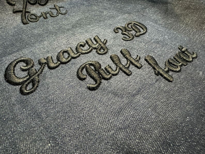 May include: Black embroidered text on a blue fabric background. The text reads "Gracy 3D Puff Font".